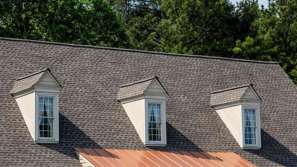 A gray shingled roof with three forward-facing windows installed by American Home Contractors New Jersey.