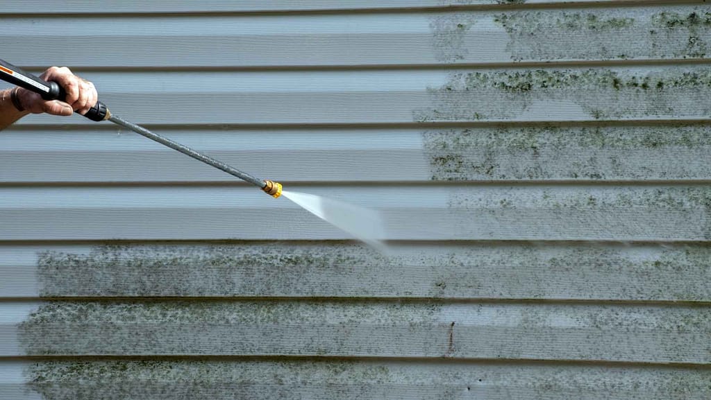 Person using pressure washer to clean vinyl siding