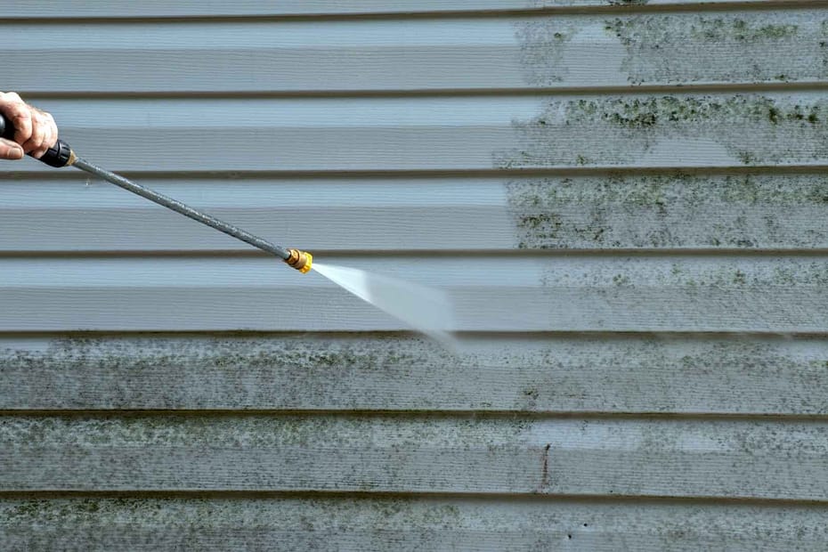 Person using pressure washer to clean vinyl siding